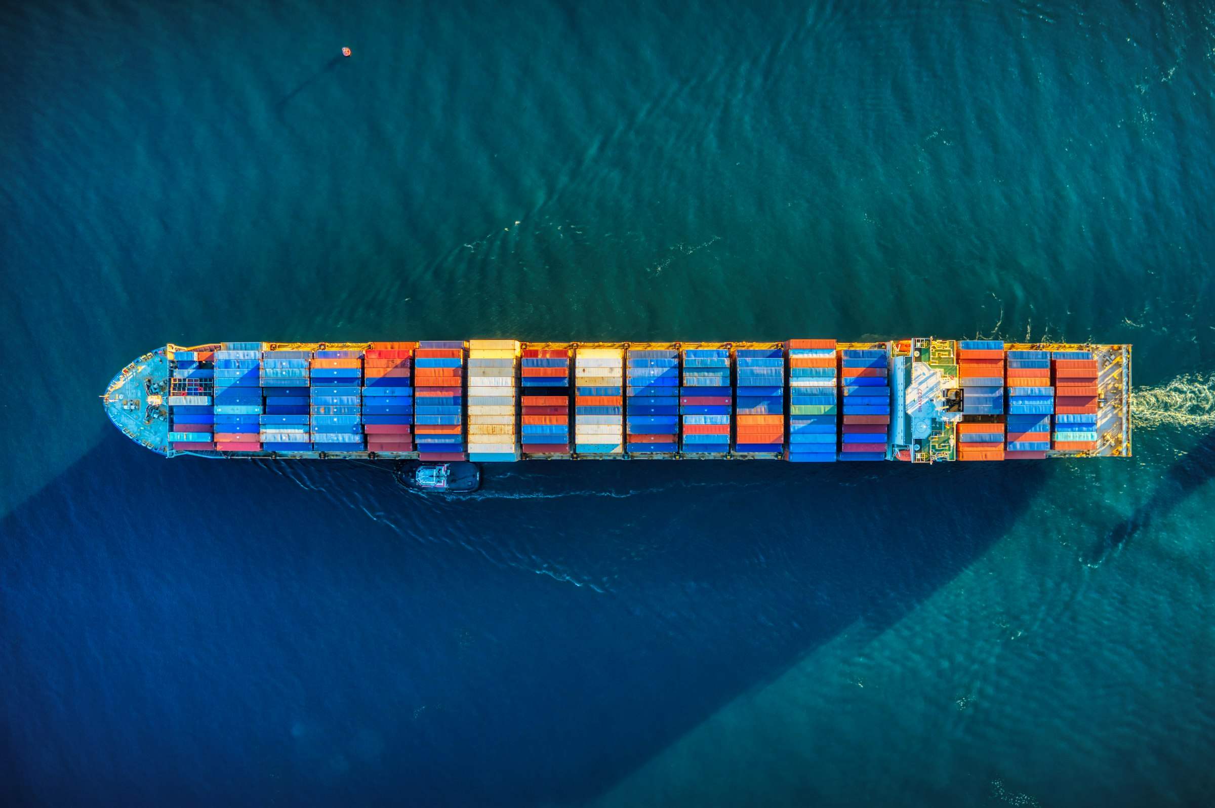 A container ship loaded with containers crossing open water, seen from above